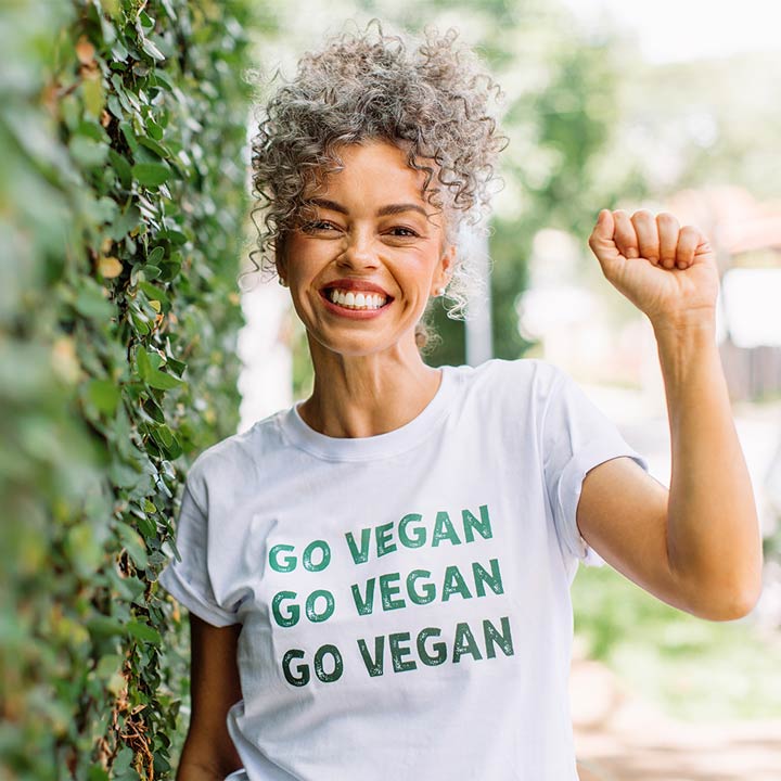 Eine Frau trägt ein T-Shirt mit dem Aufdruck "Go Vegan" und hebt die geballte Hand.